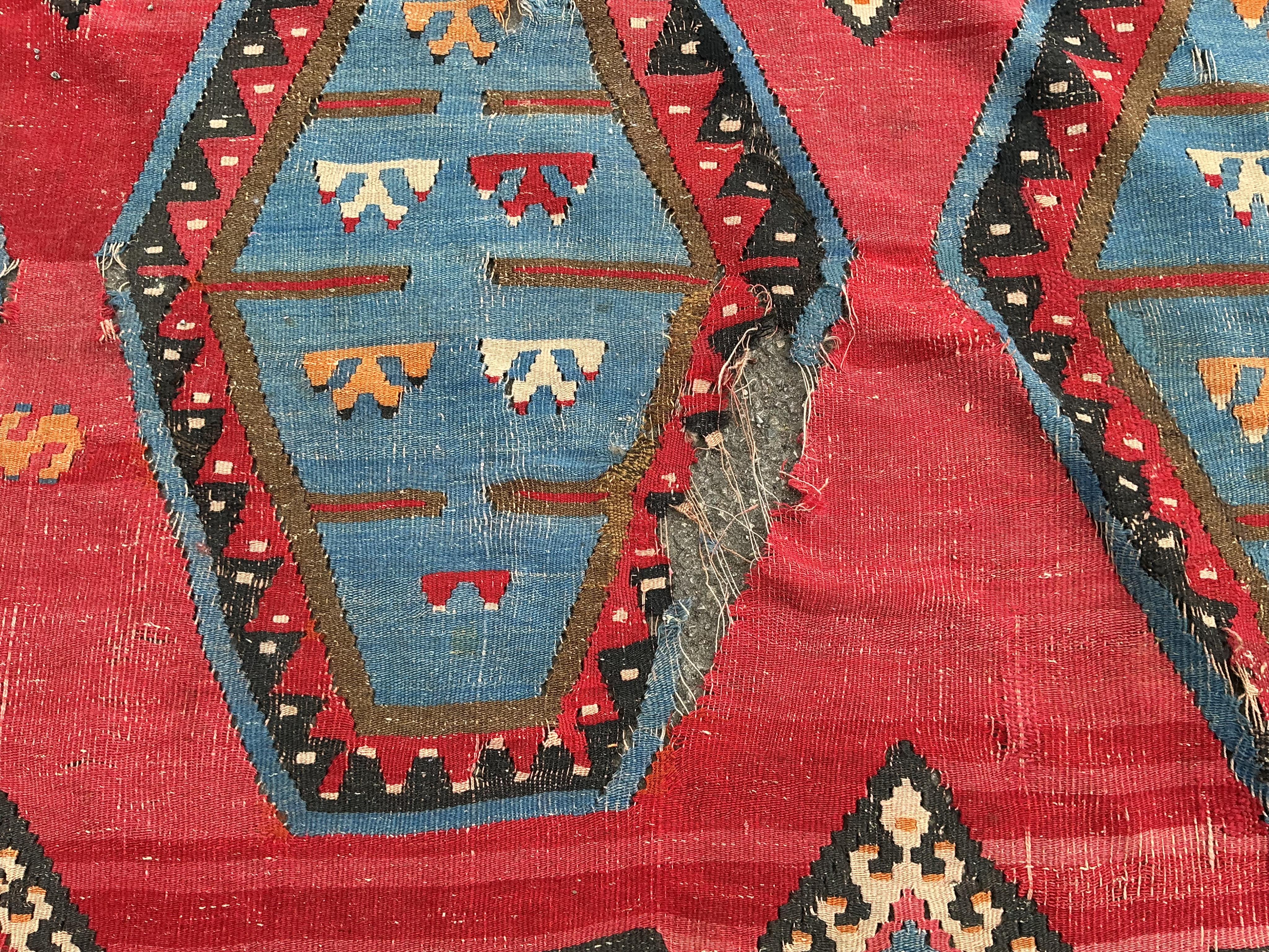 A Turkish Kilim flatweave polychrome carpet, woven with three rows of hexagons, on a red ground, (severely holed and damaged in places), 373 x 267cm